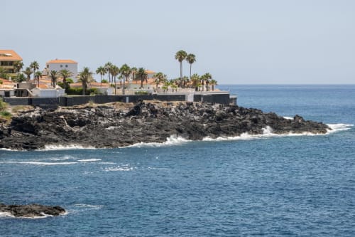 Coastal cliffside hotel with palm trees and terracotta roofs overlooking turquoise sea in Costa Adeje, Tenerife