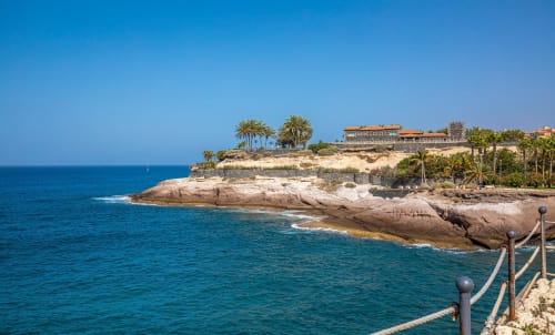 Coastal cliffs with palm trees and buildings in Costa Adeje, Tenerife overlooking turquoise Mediterranean waters