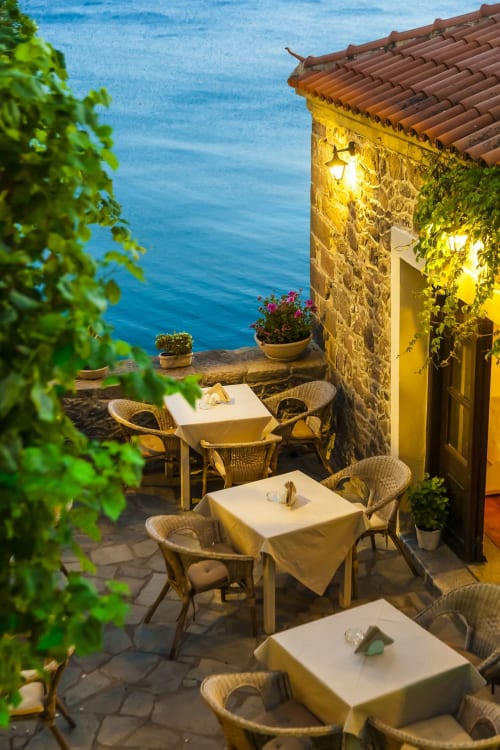 Seaside terrace dining at Marigold Costa Adeje with stone building, wicker chairs, and azure sea views