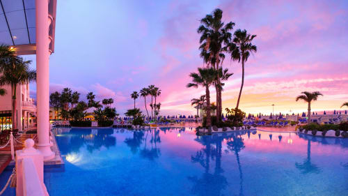 Sunset over illuminated pool at Costa Adeje resort with palm trees and loungers