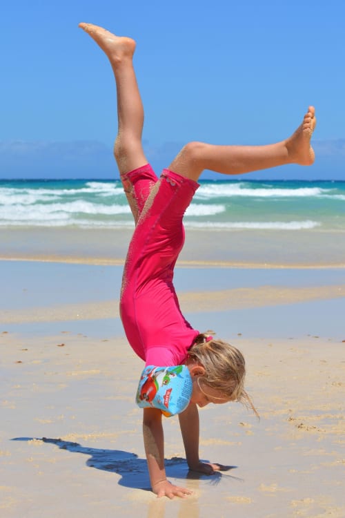 Young child doing handstand on beach in pink swimsuit, Costa Adeje Tenerife