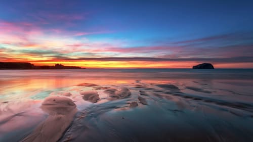 Stunning sunset over Costa Adeje beach with golden sky reflections on wet sand and calm ocean waters