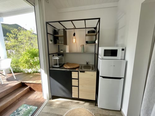 Kitchenette moderne dans un studio à Saint-Martin avec étagères à cadre noir, appareils blancs et accès à vue montagne par baie vitrée
