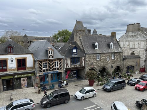 Bâtiments médiévaux en pierre et architecture à colombages sur la place de Dol de Bretagne avec voitures garées et commerces