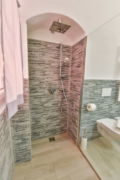 Bagno moderno con doccia rivestita in piastrelle effetto legno, box in vetro e sanitari bianchi nell'appartamento di Varigotti