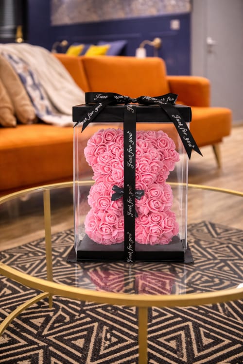 Ours en peluche rose avec fleur dans boîte transparente et ruban noir dans suite moderne du SPA LE CLANDESTIN Cambrai