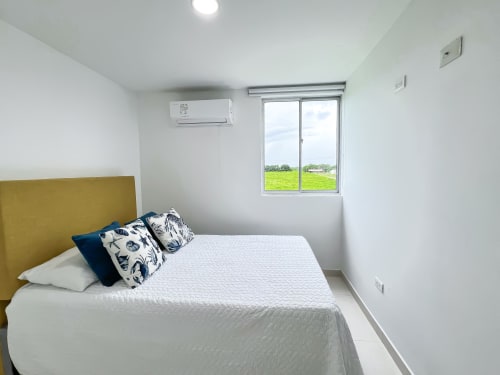 Moderna habitación con cabecero en oliva, vista al lago, aire acondicionado y paisaje verde de campiña en Olamar Living Coveñas