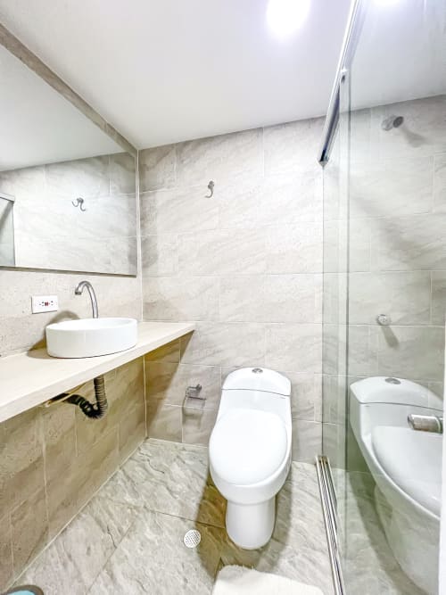Baño moderno en el hotel Olamar Living de Coveñas con inodoro blanco, lavabo redondo, azulejos de mármol y ducha con cristalería
