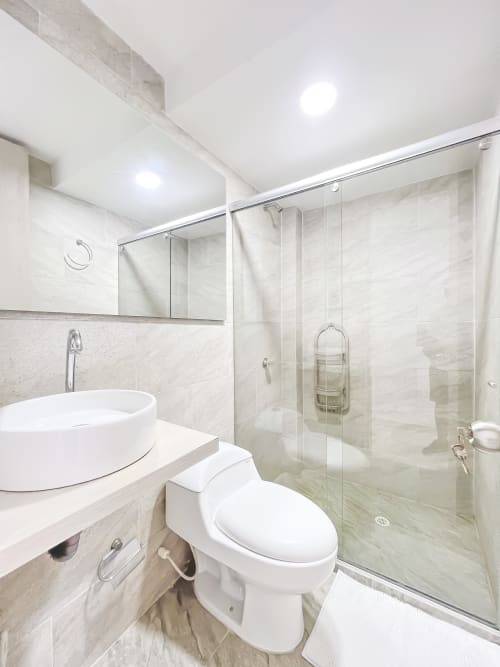 Baño moderno en apartamento Olamar Living con lavabo de porcelana, inodoro y ducha con cabina de vidrio en tonos mármol neutros