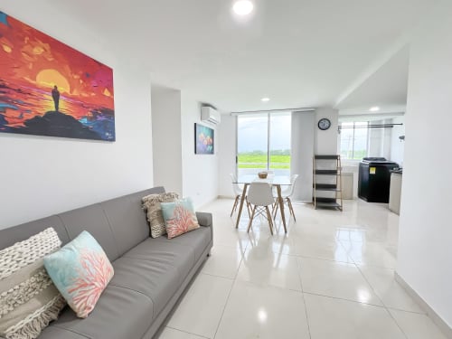 Moderno apartamento Caribe en Olamar Living con sofá gris, comedor, cocina americana y vista al lago desde el balcón.