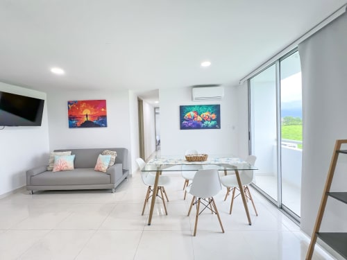 Moderno salón con sofá gris, mesa de comedor, obras de arte coloridas, aire acondicionado y puertas corredizas de cristal