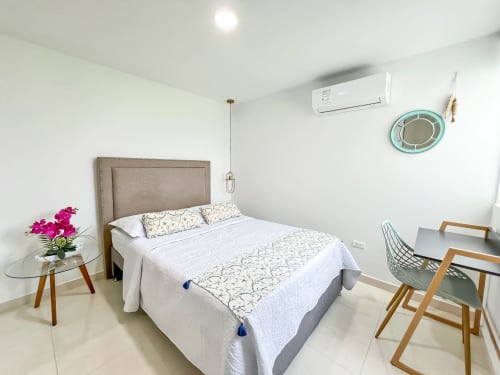 Habitación moderna del hotel Olamar Living en Coveñas con cama queen, aire acondicionado, espejo turquesa y sillas de madera