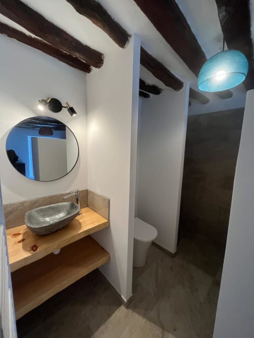 Salle de bain moderne de la villa Brando avec miroir rond, vasque sur comptoir en bois, sol sombre et luminaire suspendu bleu