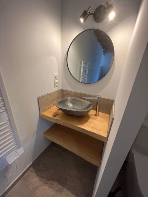 Salle de bain moderne avec vasque en pierre, plan de travail en bois, miroir rond et éclairage d'accent à la villa Altezza, Brando