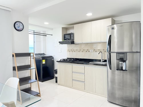 Cocina moderna en apartamento de Coveñas con electrodomésticos de acero inoxidable, gabinetes blancos, encimera negra y área de comedor