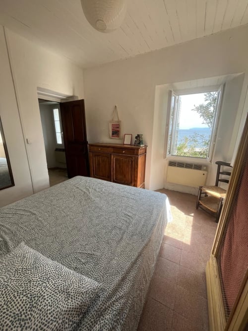 Chambre lumineuse avec vue sur mer à la villa Altezza à Brando, Corse, avec lit, mobilier bois et paysage côtier