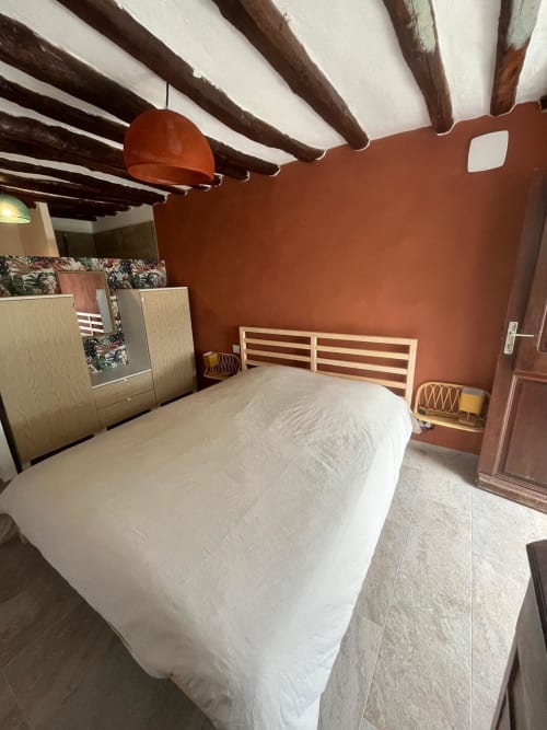 Chambre rustique avec poutres apparentes, murs en terre cuite, lit en bois et literie blanche à la villa Altezza à Brando