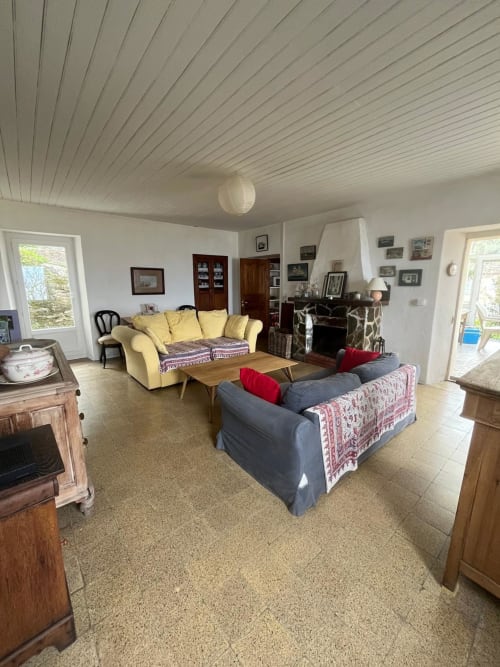 Spacieux séjour de la villa Altezza à Brando avec canapé jaune, assises bleues, cheminée et vue sur la mer par les portes-fenêtres