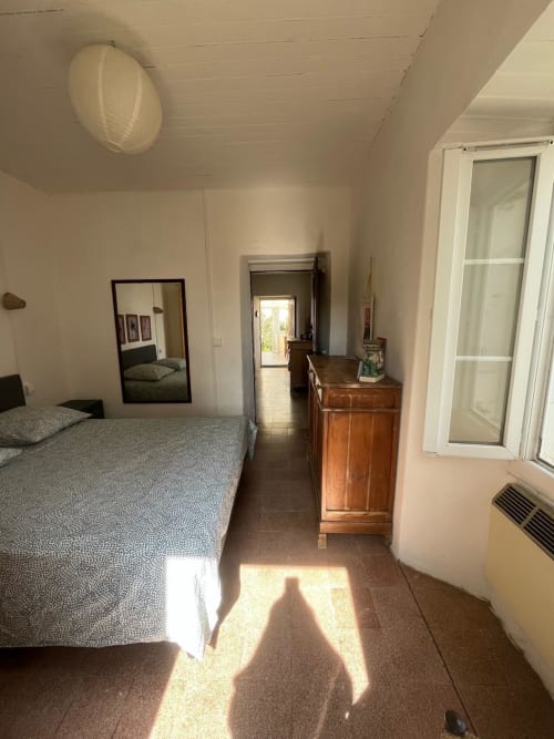 Chambre lumineuse de la villa Brando avec lit, commode en bois et vue sur la mer par les portes ouvertes