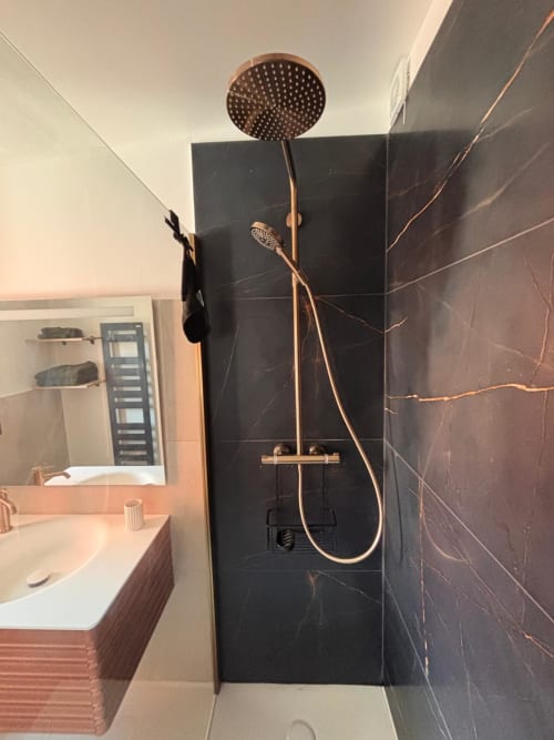 Salle de bain moderne avec douchette pluie, robinetterie bronze et murs en marbre noir à l'hôtel Altezza à Brando
