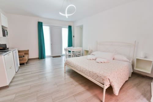 Camera moderna dell'hotel VARIGOTTI FABIO con biancheria rosa, cornice letto bianca, angolo cottura e tende turchesi