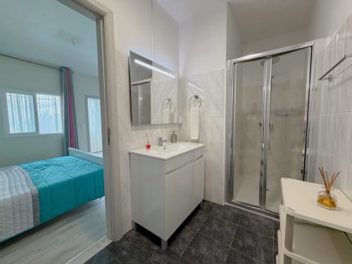 Modern bathroom with vanity sink, mirror, shower enclosure, and view to turquoise bed at Isabella's House villa in Ribeira
