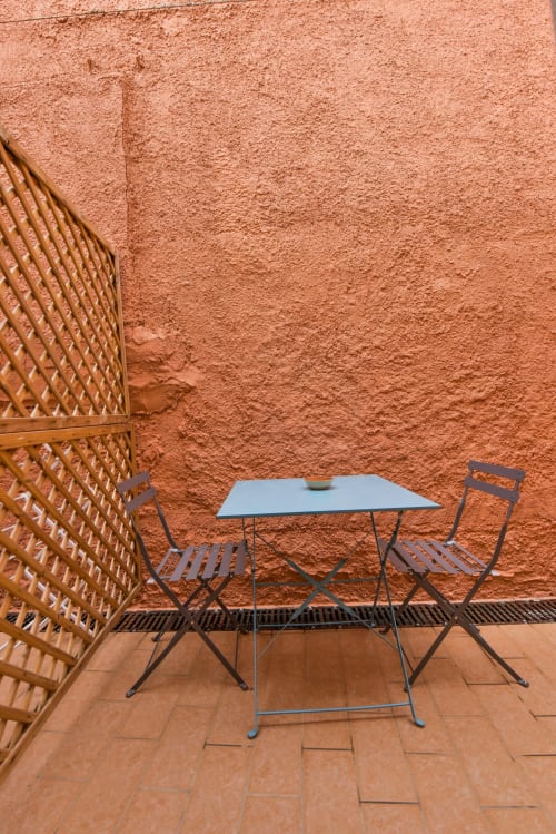 Terrazza minimalista in terracotta dell'appartamento Varigotti Fabio con tavolo blu in metallo, sedie e schermo in vimini intrecciato