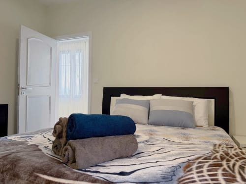Quarto moderno do hotel Check Madeira em Ribeira Brava com cama, almofadas, toalhas dobradas e porta para varanda