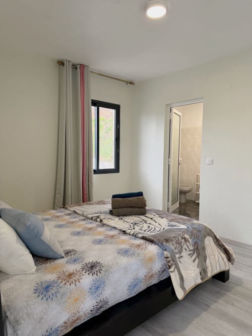 Quarto moderno do hotel Check Madeira em Ribeira Brava com roupa de cama estampada, janela e casa de banho privativa