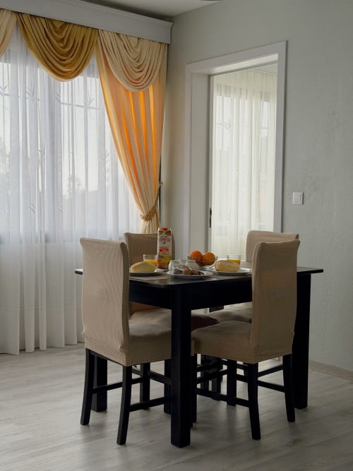 Área de refeições do hotel Check Madeira em Ribeira Brava com mesa preta, cadeiras bege e elegantes cortinas douradas