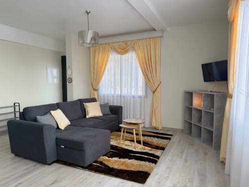Sala de estar moderna do hotel Check Madeira em Ribeira Brava com sofá escuro, cortinas douradas e TV de ecrã plano