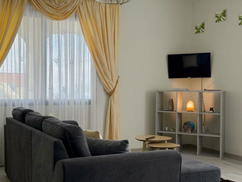 Sala de estar moderna no hotel Check Madeira em Ribeira Brava com sofá escuro, TV de parede e cortinas douradas