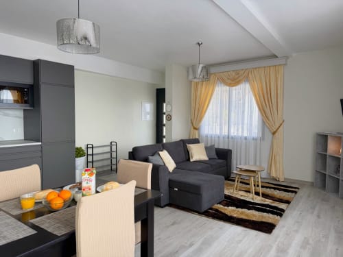 Moderno estúdio em Check Madeira, Ribeira Brava, com sofá preto, sala de jantar, kitchenette e cortinas douradas.