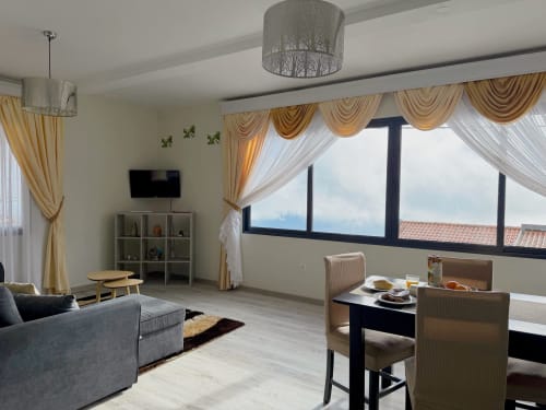 Moderno estúdio no Check Madeira em Ribeira Brava com vista oceânica, sofá cinzento, zona de refeições e cortinados dourados