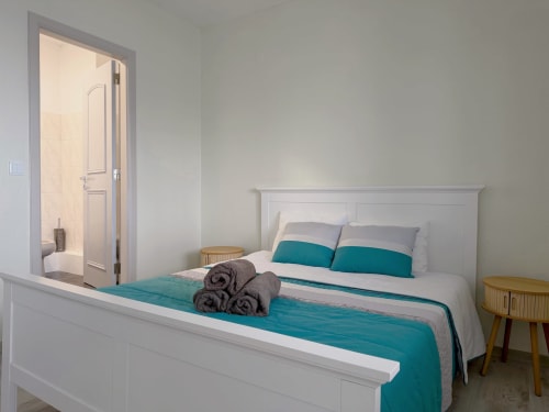 Quarto moderno no Check Madeira com cama queen, roupa de cama turquesa, toalhas enroladas, banheiro privativo e criados em madeira,