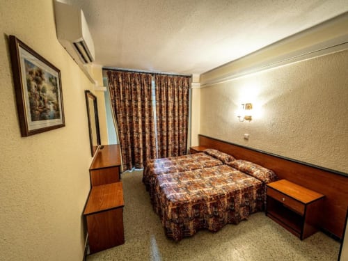 Habitación doble en Hotel Continental Calella con camas gemelas, muebles de madera y vistas al patio interior a través de las cortinas