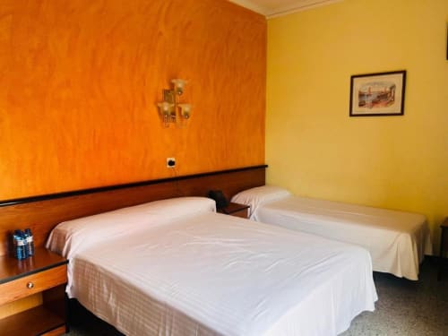 Habitación Familiar del Hotel Continental Calella con dos camas, paredes naranja y amarillas, cabecero de madera y comodidades modernas