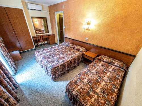 Habitación Triple Clásica del Hotel Continental Calella con dos camas, muebles de madera y paredes texturizadas en naranja