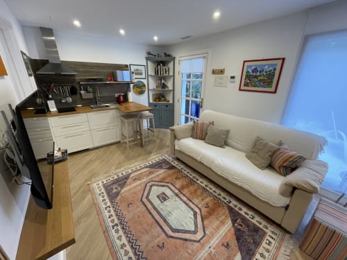 Sala de estar de villa moderna de planta abierta con sofá crema, cocina, suelos de madera y vistas a las montañas en Playa Blanca, Lanzarote