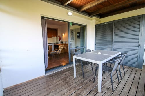 Área de jantar externa da Villa Alegria com mesa branca, espreguiçadeiras e vista para o oceano através das portas do pátio aberto em Zonas