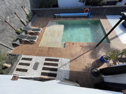 Vista aérea de la piscina de la villa Playa Blanca con tumbonas, patio de terracota y vistas a las montañas