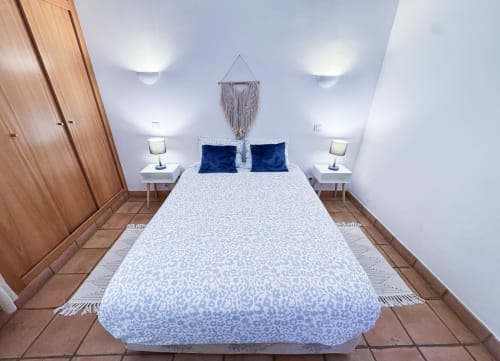Quarto moderno da Villa Alegria em Lagos com roupa de cama azul estampada, almofadas azul-marinho, mesas laterais brancas e acabamentos em madeira quente