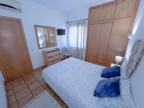 Quarto da Vila Alegria em Zonas Mágicas, Lagos - cama de casal com almofadas azuis, móveis em madeira, TV e comodidades modernas