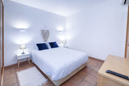 Quarto moderno na Villa Alegria, Zonas Mágicas Lagos com cama queen, almofadas azul-marinho, arandelas de parede e piso em terracota