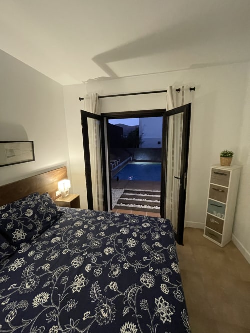 Dormitorio moderno con vistas a la piscina, puertas que se abren a la terraza de la villa Playa Blanca con vistas a las montañas y amenidades al aire libre