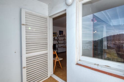 Habitació d'hotel modern a Finques Garcia Enrich amb porta de lames blanques, cadira de fusta, estanteries i vistes panoràmiques costaneres
