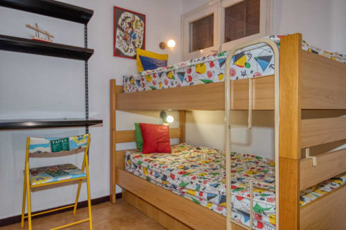 Dormitori infantil colorit amb llits beç de fusta i emmagatzematge de joguines a l'hotel Finques Garcia Enrich a Palafrugell.