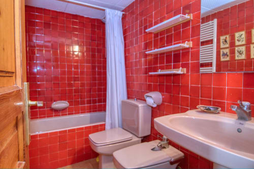 Bany de rajoles rojo brillant amb dutxa, vàter, lavabo i estanteries a l'hotel Finques Garcia Enrich a Palafrugell