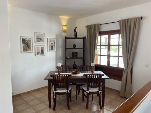 Elegante comedor en Villa Pola Marinas, Playa Blanca con mesa de madera, sillas, estanterías y vistas al mar a través de amplios