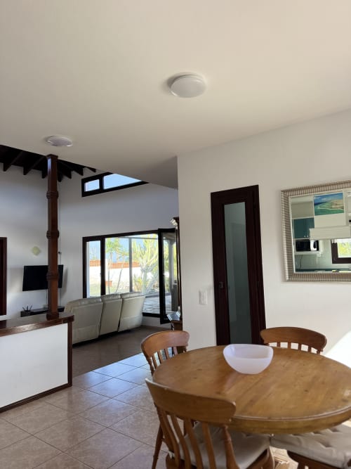 Comedor de villa moderna con mesa de madera, vistas al océano a través de puertas de cristal y diseño abierto luminoso en Corralejo